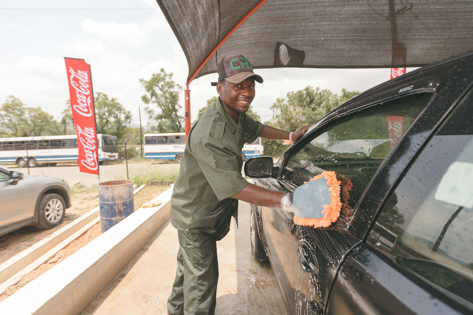 A MAPS Village attendant washing a black car under the wash canopy